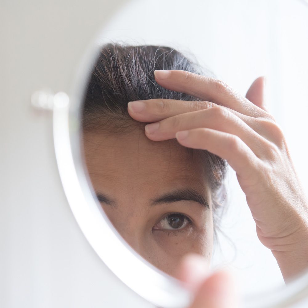 woman examines hair in the mirror